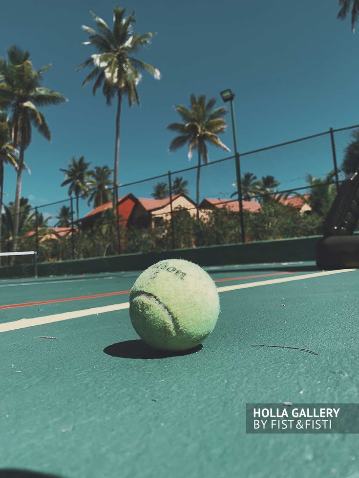 Мяч на теннисном корте на фоне коттеджей и высоких пальм Доминиканской Республики