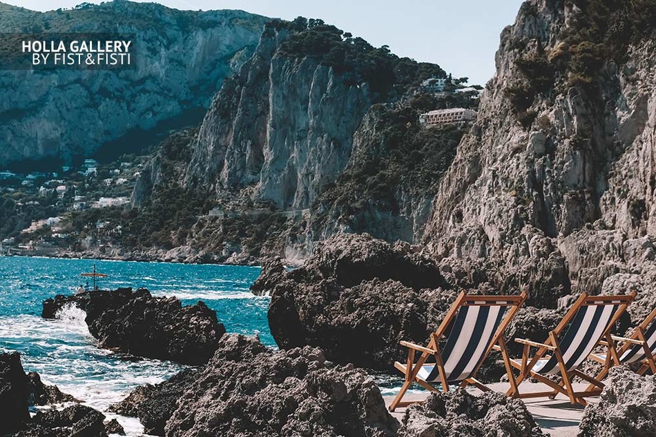 Пляж с шезлонгами среди скал в заливе на Капри в Италии