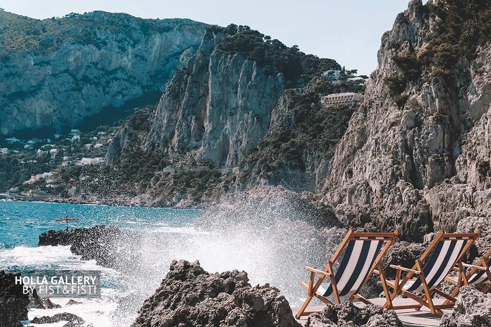 Брызги воды на пляже с шезлонгами среди скал в заливе на Капри в Италии, фото картина